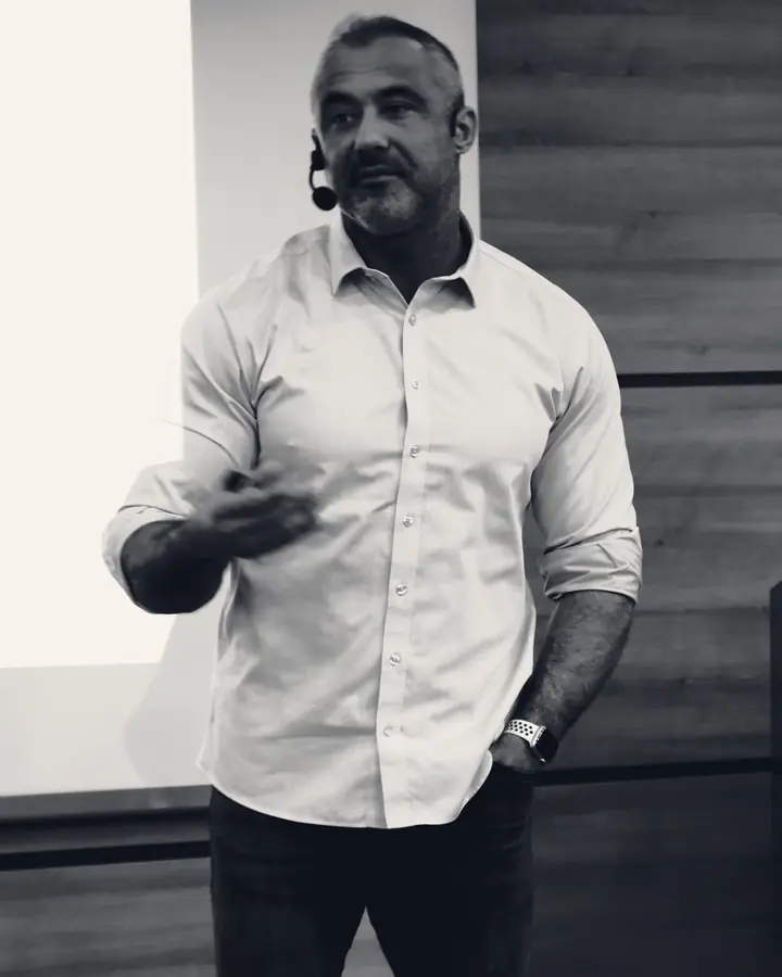Mehmet Safa Yalçıntaş kürsüde, kafa mikrofonuyla anlatırken gülümsüyor