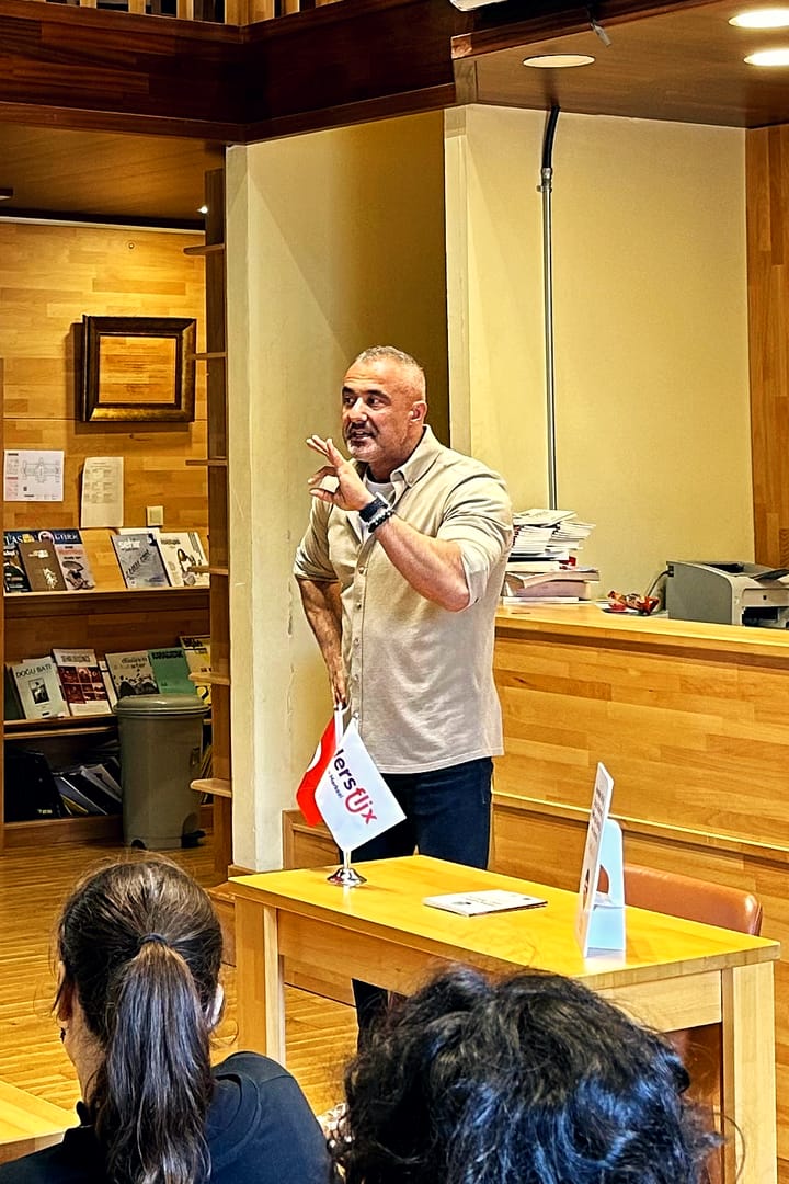 Mehmet Safa Yalçıntaş, bir okul kütüphanesinde kitap raflarının önünde anlatırken